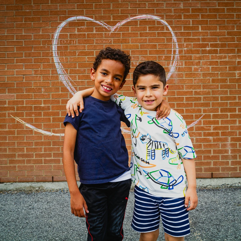 deux petits garçons devant le mur de l'école sur lequel un coeur en craie est dessiné