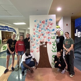 élèves qui font la pose devant un grand bricolage pour la journée de la terre, des mains dans la peinture font les branches d'un arbre