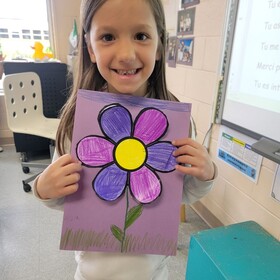 une élève souriante avec son dessin de fleur mauve